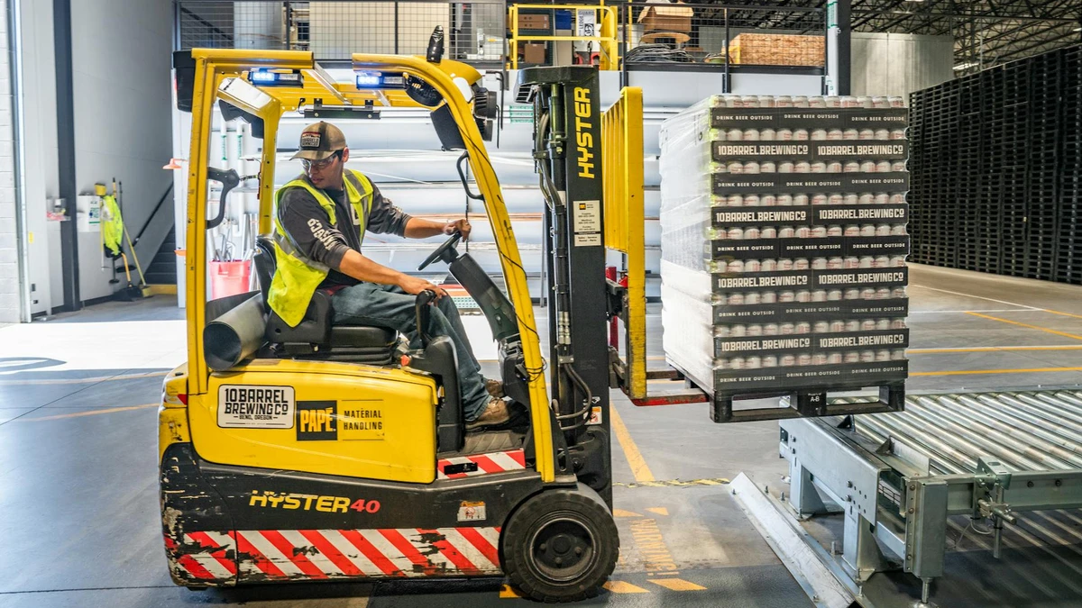 Papacko Warehouse worker operating forklift loading pallets of paper cups onto shipping container