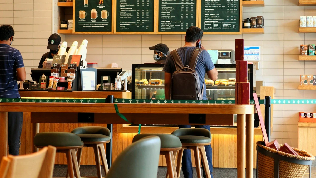 Papacko Busy coffee shop counter with barista serving customers using branded paper cups, showcasing modern 