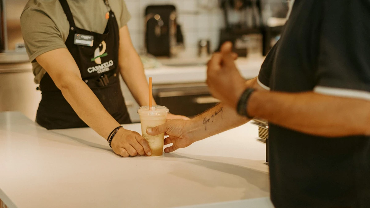 Cafe staff serving cold beverage in compostable cup to satisfied customer